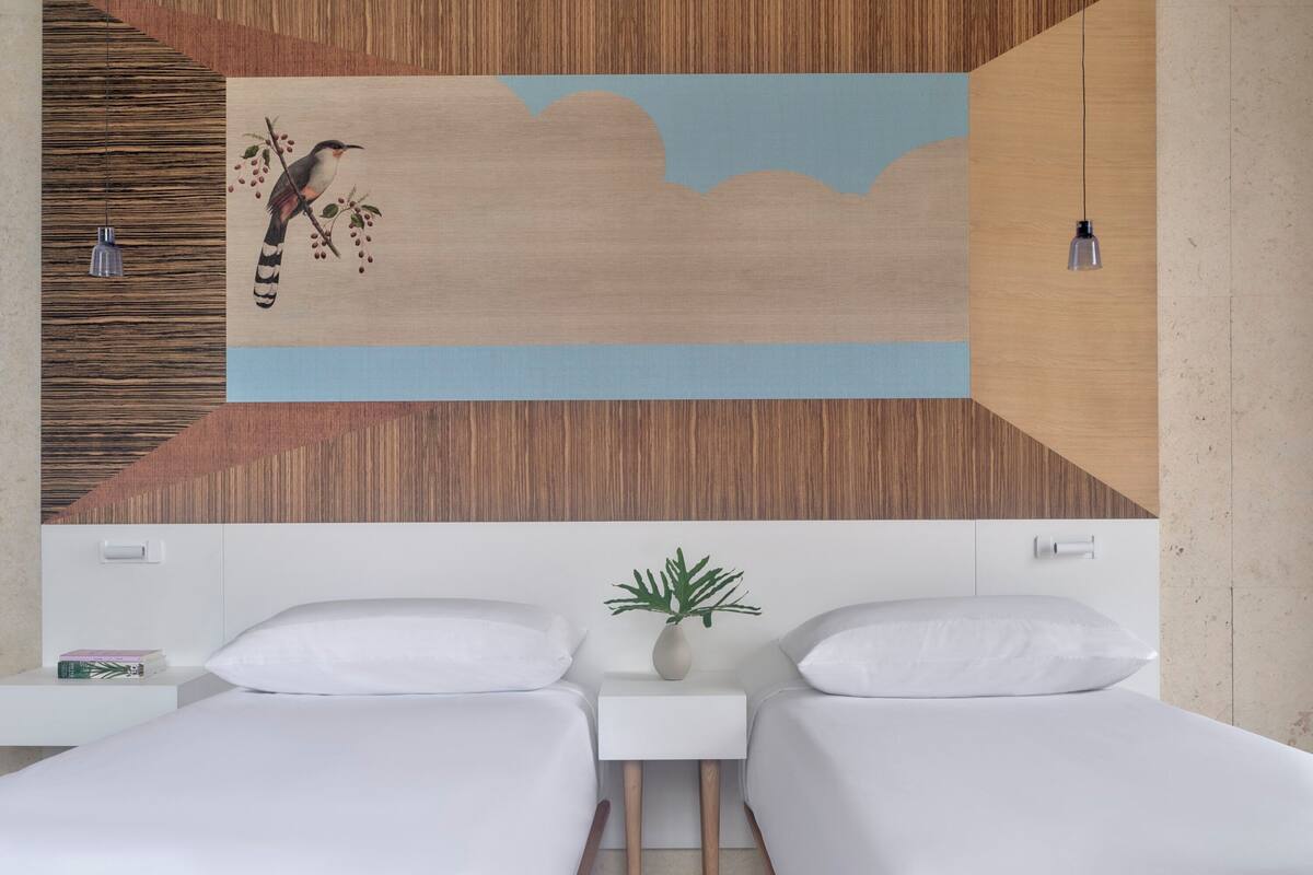 Moderni hotellihuone, jossa on kaksi sänkyä, puusta tehty koristeellinen seinä, lintukuva, pieni kasvi ja riippuvalaisin.