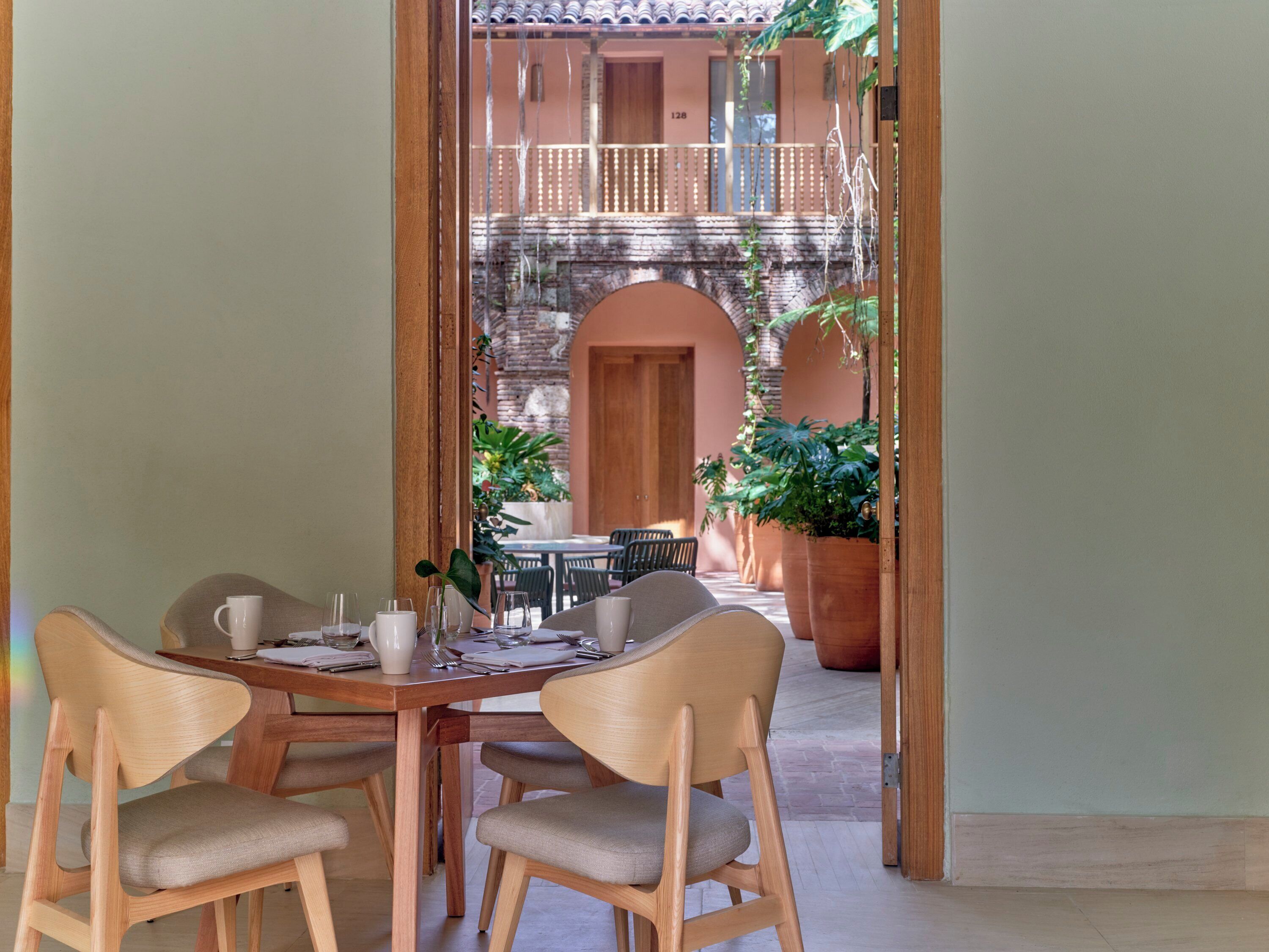 Un coin repas avec une table et des chaises en bois, donnant sur une terrasse extérieure agrémentée d’un mur en briques et de plantes en pot.