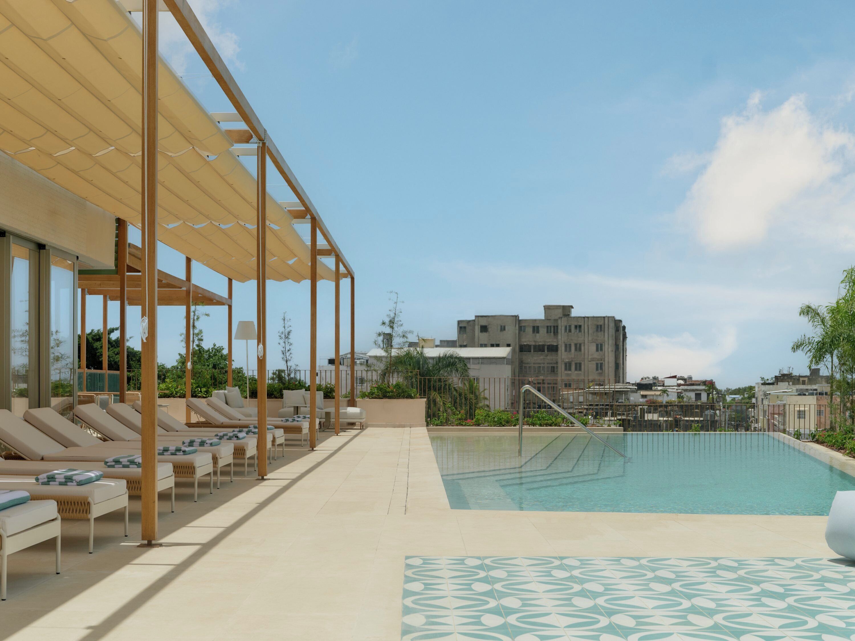 A rooftop pool area with sun loungers and a pergola providing shade.