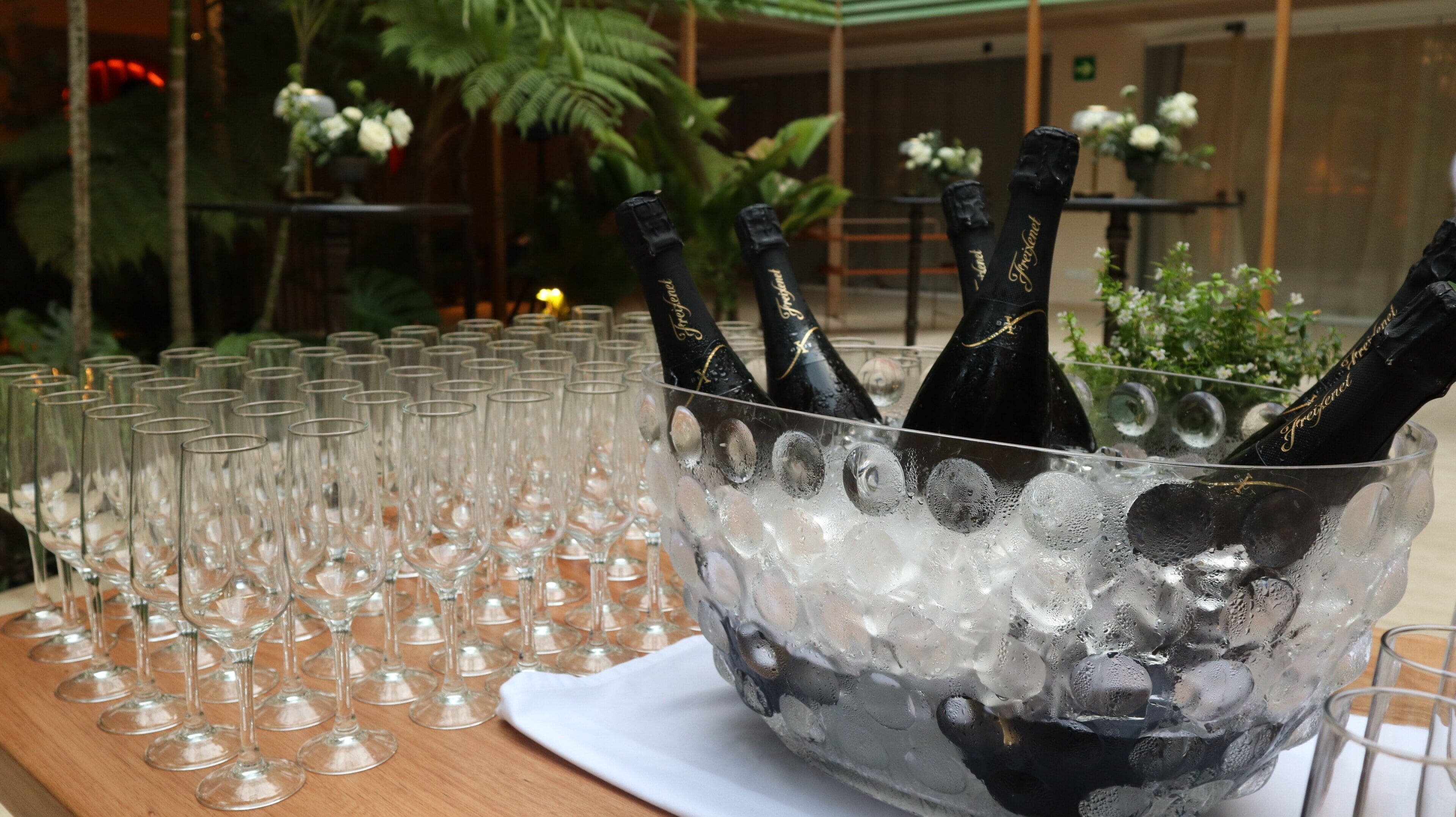 A table with a large ice-filled bowl containing champagne bottles and numerous empty wine glasses.