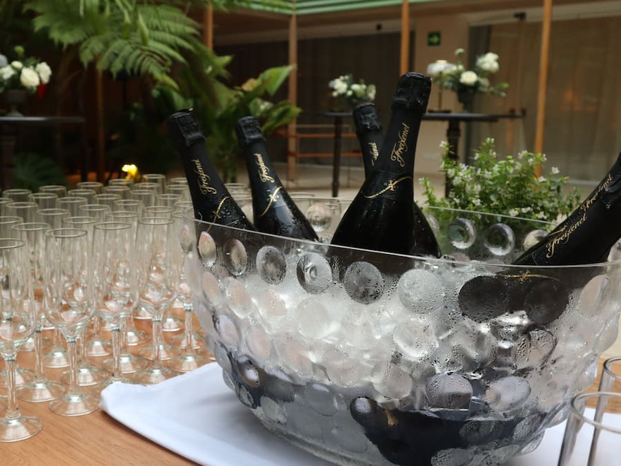 A table with a large ice-filled bowl containing champagne bottles and numerous empty wine glasses.