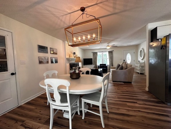 A modern kitchen with a round dining table, white chairs, and a hanging light fixture.