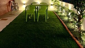 A small outdoor patio area with a green lawn, a table with chairs, and a brick wall. - Your getaway home with Ganga view in Rishikesh (Rishikesh)