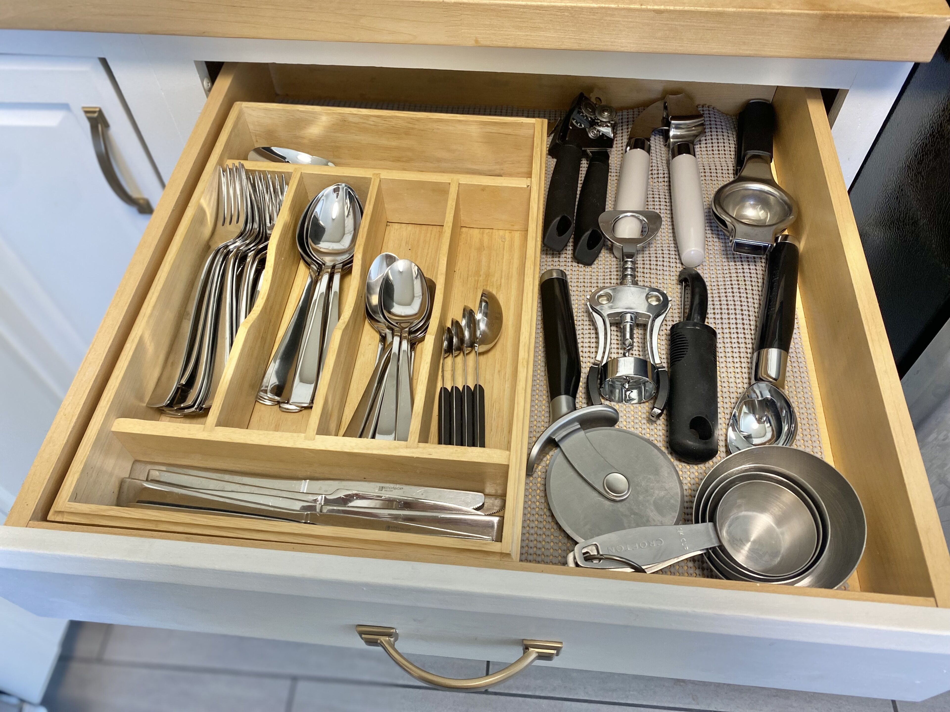 A drawer with neatly organized kitchen utensils including spoons, forks, knives, and a grater.