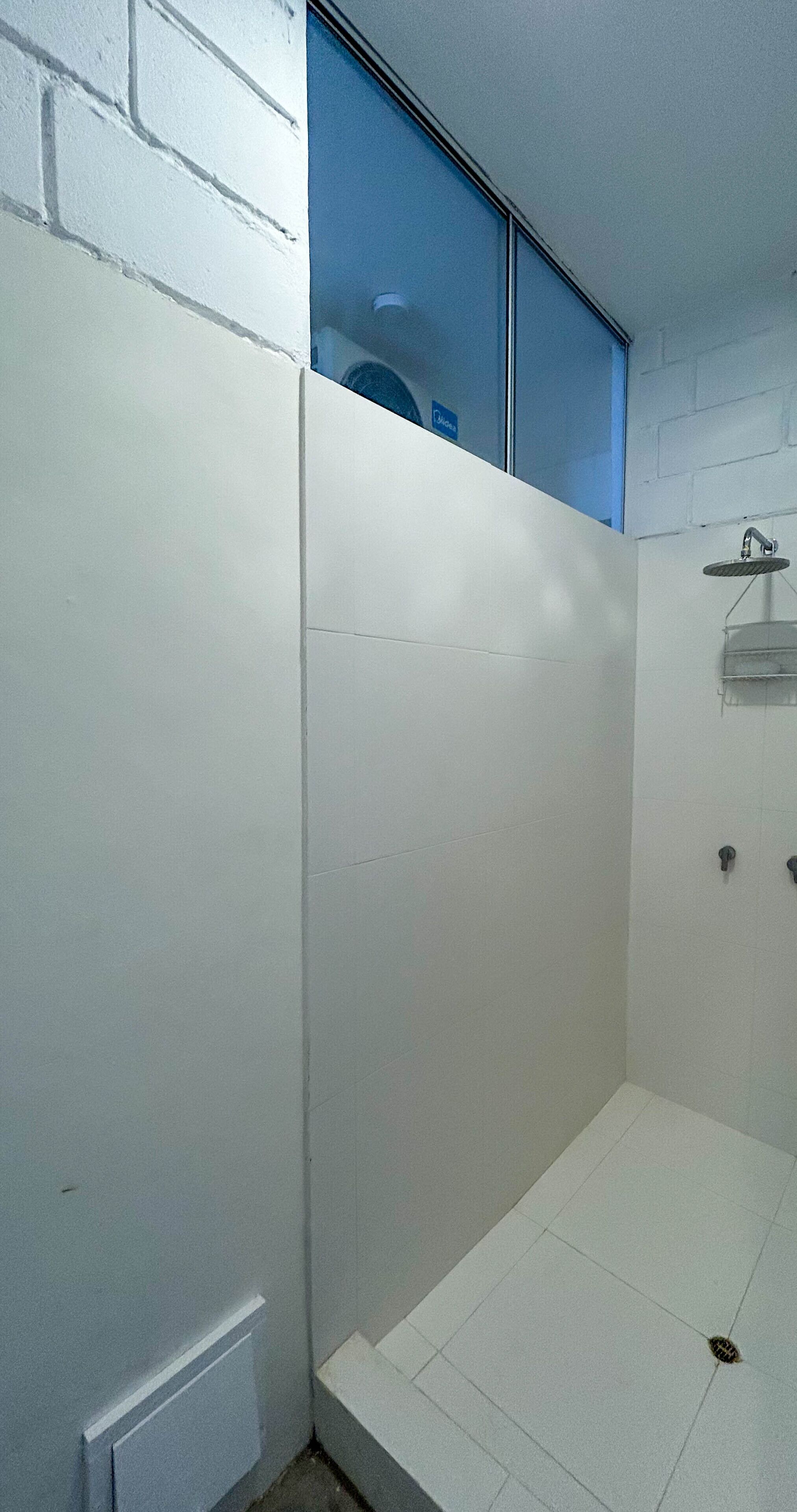 Un baño pequeño con paredes blancas, zona de ducha, una ventana y una puerta.
