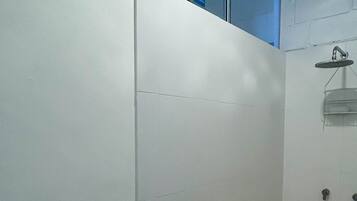 Un baño pequeño con paredes blancas, zona de ducha, una ventana y una puerta.