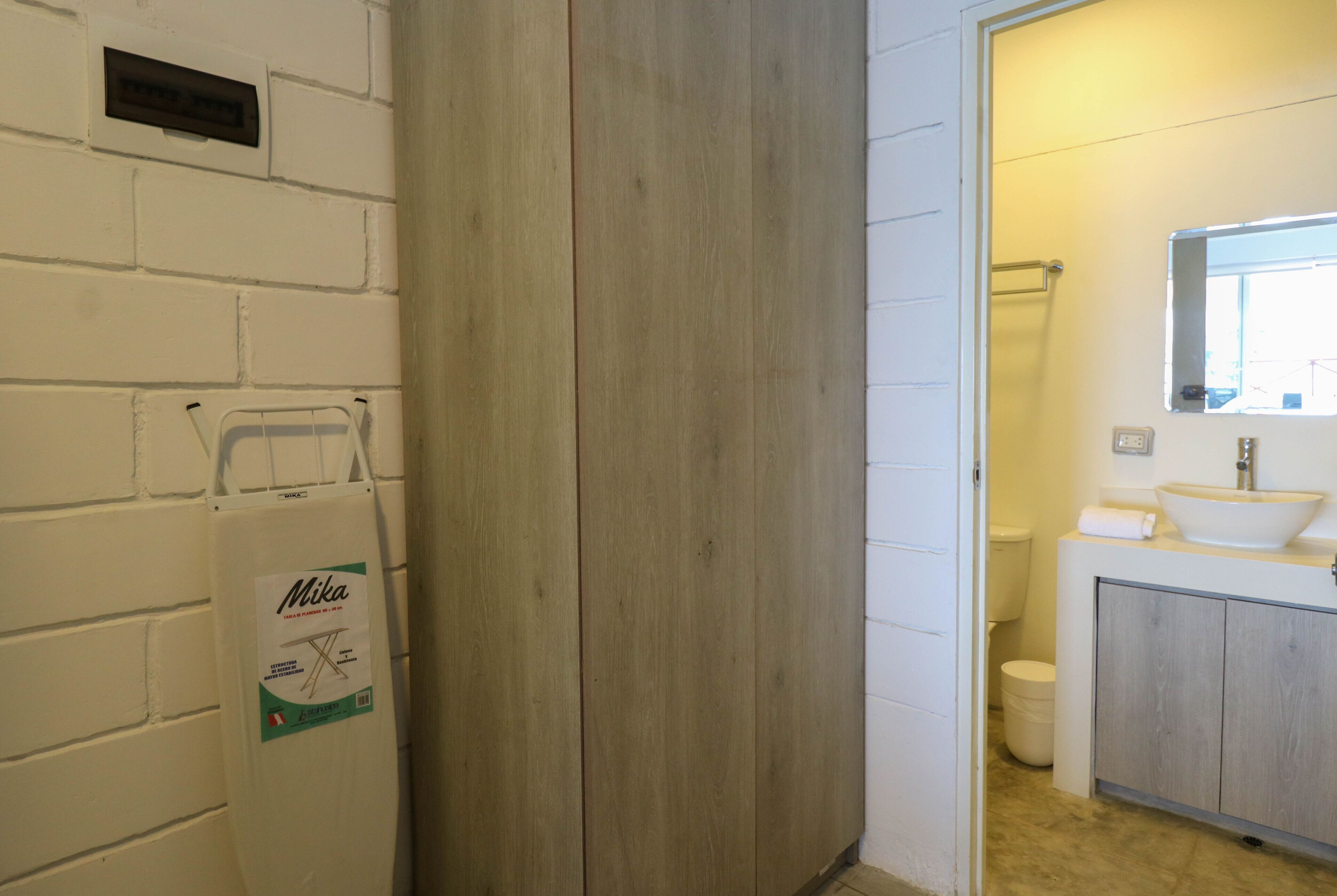Een badkamer met een houten scheiding, een wit wastafelmeubel en een spiegel erboven.