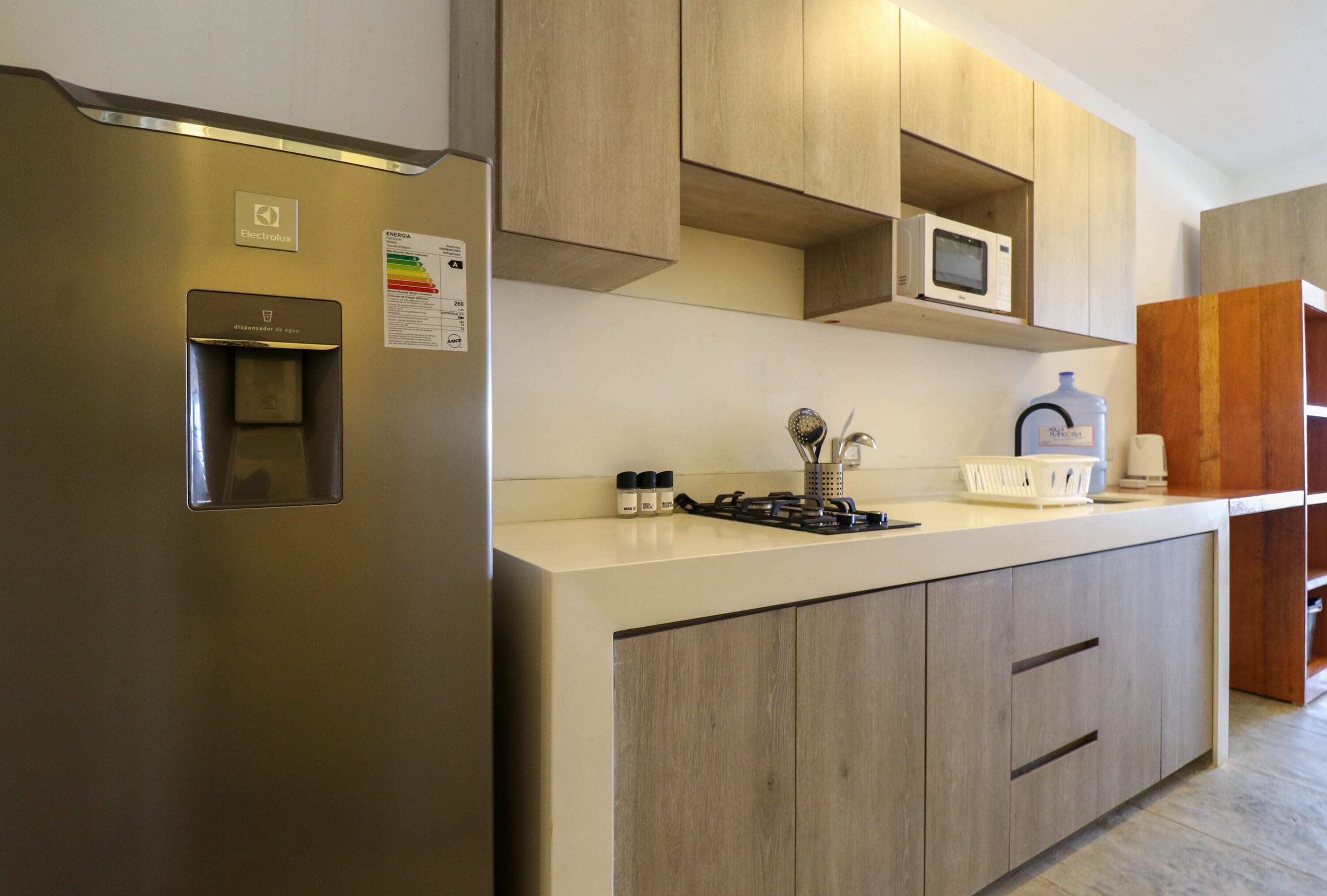 A modern kitchen with a stainless steel refrigerator, wooden cabinets, a microwave, and a gas stove.