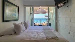 Une chambre avec un lit, un téléviseur fixé au mur et une vue sur la mer, visible à travers une porte ouverte.