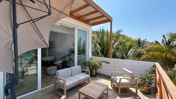 Een balkon met een bank, stoelen, een klein tafeltje en potplanten.