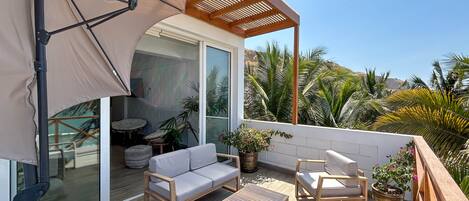 A balcony with a sofa, chairs, a small table, and potted plants.
