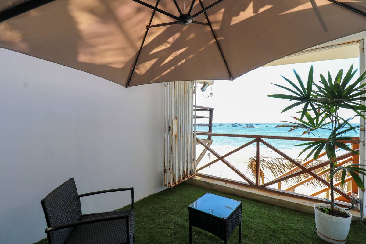 Un balcón con vista a la playa, una silla, una mesita y una planta en maceta.