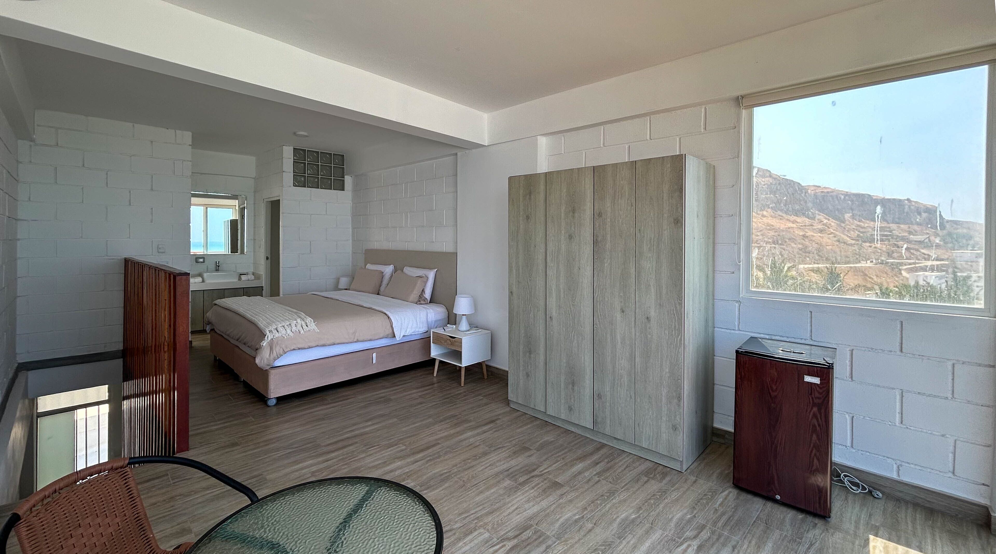 A modern bedroom with a bed, bedside table, and a view of a mountainous landscape.