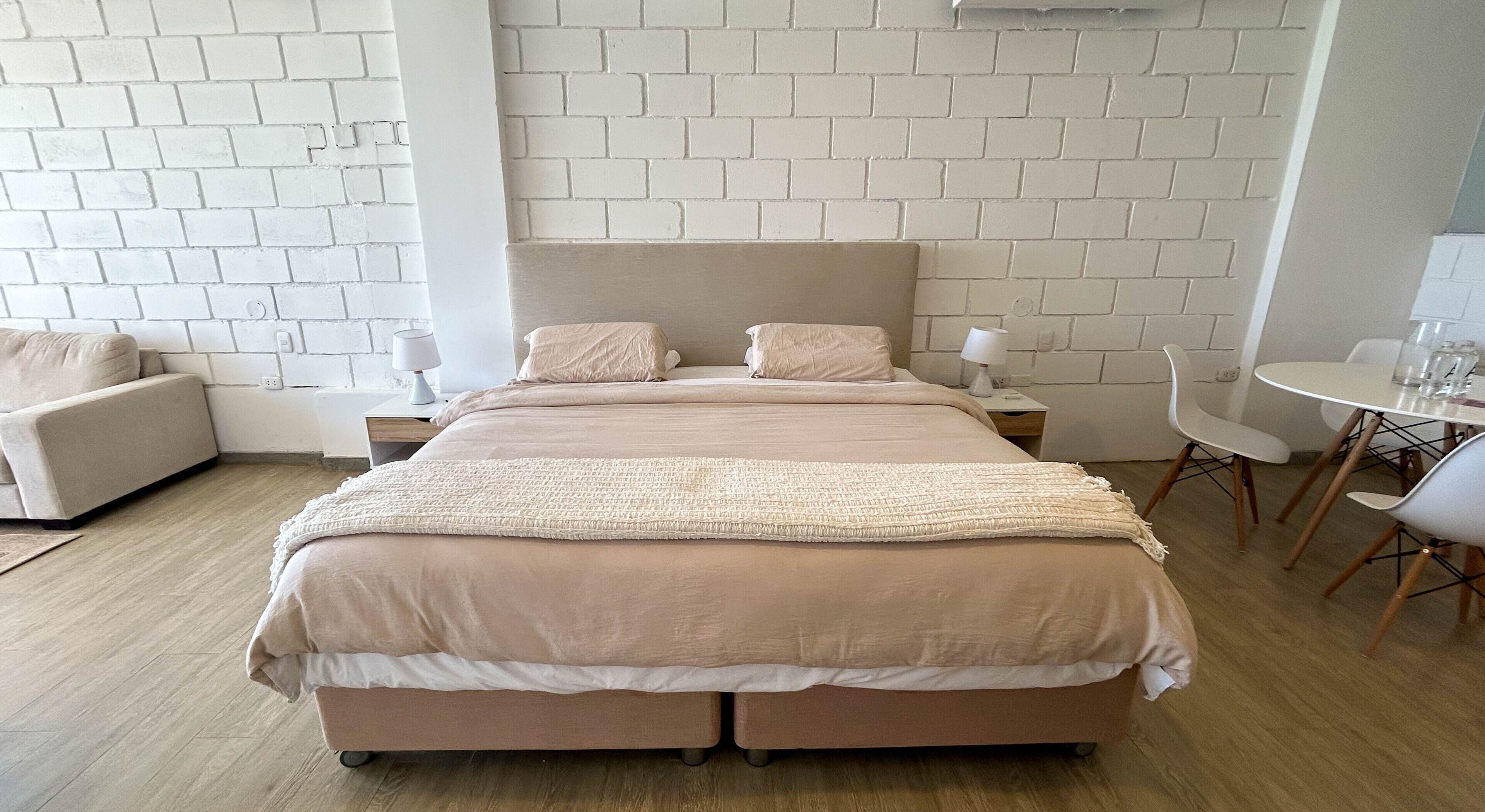 Een moderne slaapkamer met een groot bed, nachtkastjes, een stoel en een kleine tafel.
