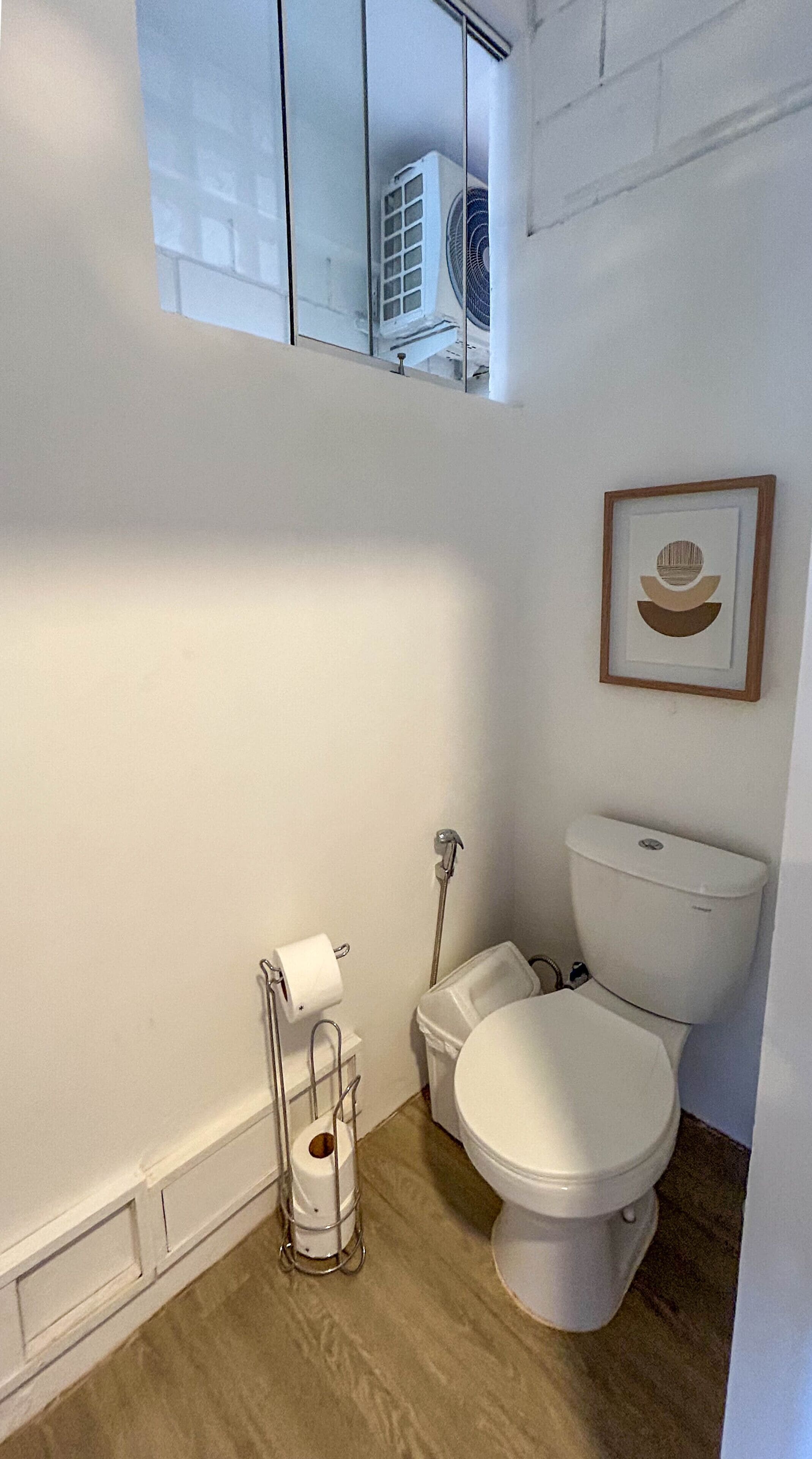 A small, clean bathroom with a toilet, a framed picture on the wall, and a window above the toilet.