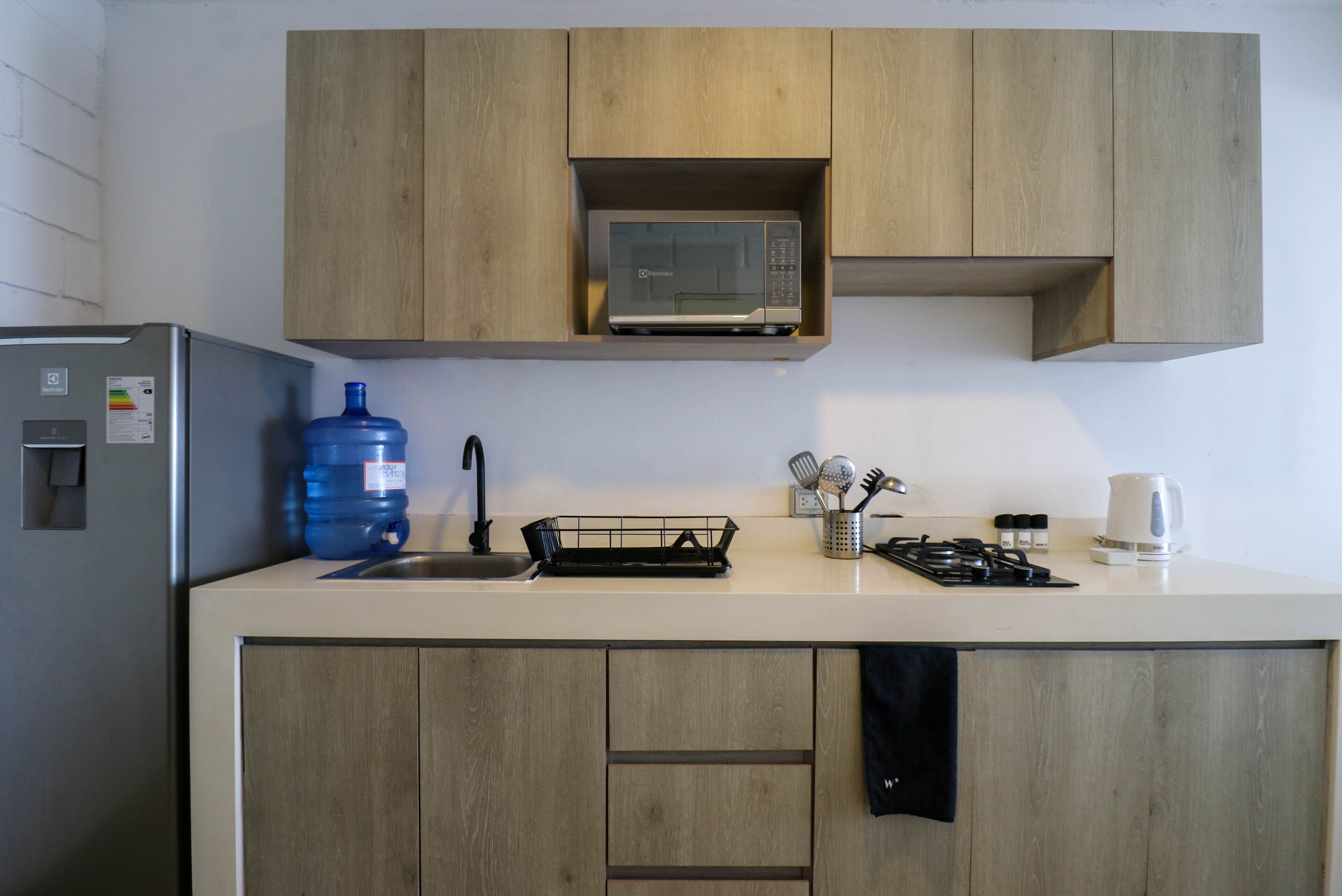 A kitchen with wooden cabinets, a microwave, a water dispenser, a sink, and a kettle.