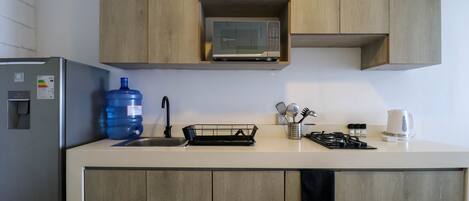 A kitchen with wooden cabinets, a microwave, a water dispenser, a sink, and a kettle.