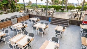 Un área de comedor al aire libre con varias mesas y sillas, una estación de buffet y vistas al mar.