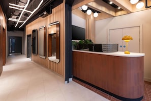 A reception desk with a wooden finish, a flat-screen TV, and a yellow lamp. - YOTELPAD London Stratford (London)