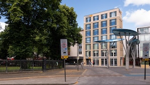 Un hôtel au design moderne, des panneaux indiquant les zones piétonnes et les pistes cyclables, et un ciel dégagé.