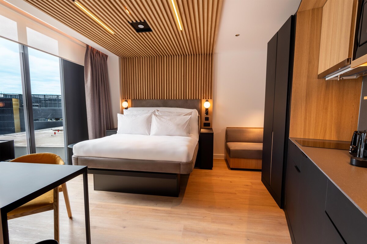 Een moderne hotelkamer met een bed, nachtkastjes, een bureau en uitzicht op buiten.