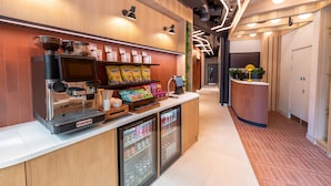 L’intérieur d’un café présente une machine à café, un présentoir de capsules de café, un réfrigérateur pour boissons et un comptoir avec une caisse enregistreuse.