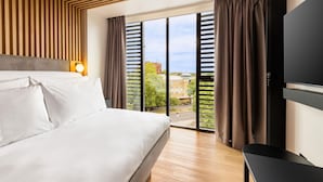 Una habitación de hotel con cama, televisor, ventana con cortinas y vistas a edificios.