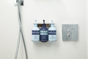 A shower with three bottles of Urban Jungle products: shampoo, conditioner, and hand & body wash. - YOTELPAD London Stratford (London)