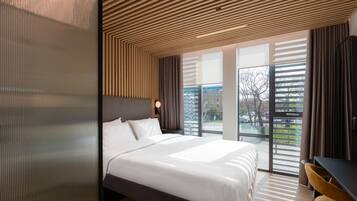 Habitación de hotel moderna con una cama grande, un escritorio y vistas a la ciudad a través de amplios ventanales.