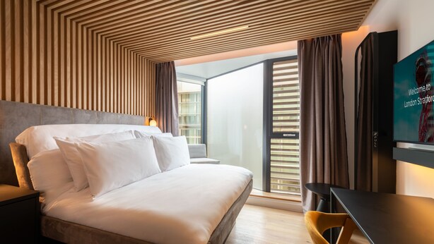 Una habitación de hotel moderna con una cama grande, un escritorio y un televisor mostrando un mensaje de bienvenida.