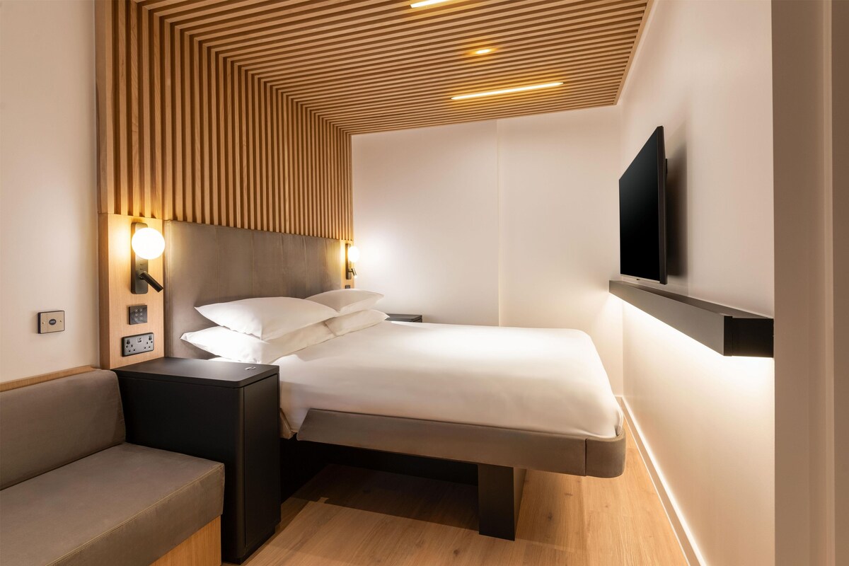 Een moderne hotelkamer met een bed, nachtkastjes, een flatscreen televisie aan de muur en een inbouwbank.