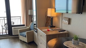 Hotellihuone, jossa on parveke, työpöytä lampun kanssa, televisio ja pieni pöytä, jonka päällä on kasvi.