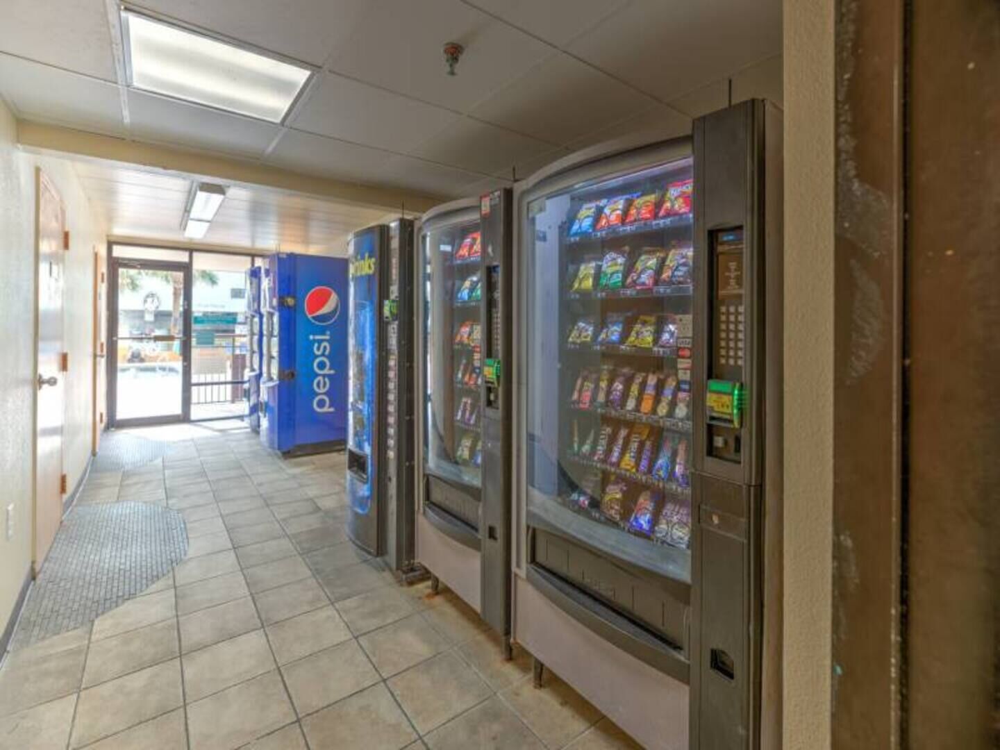 A hallway with vending machines, including a Pepsi cooler, and a tiled floor.