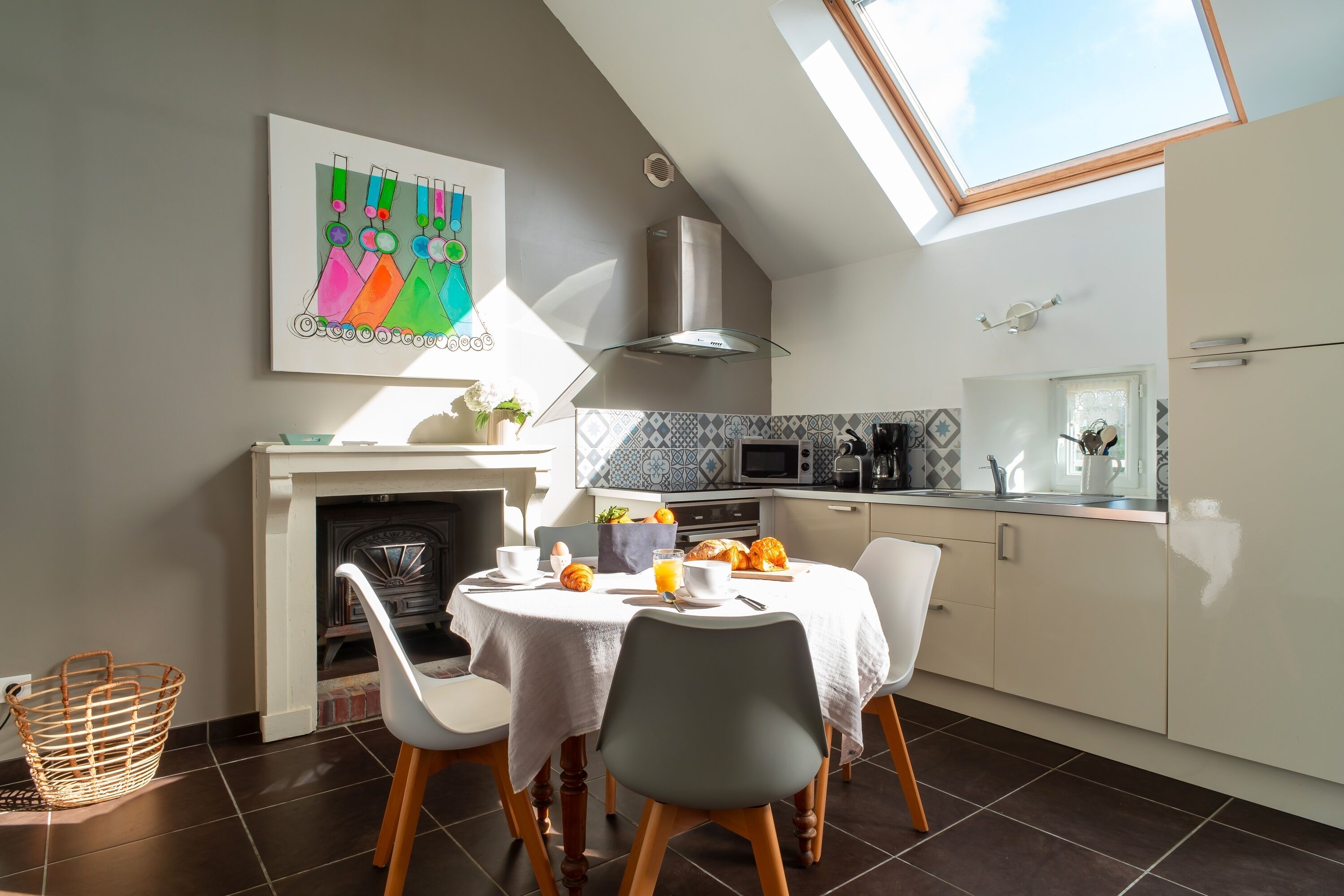 A modern kitchen with a skylight, a dining area with a white tablecloth, and a colorful abstract painting on the wall.