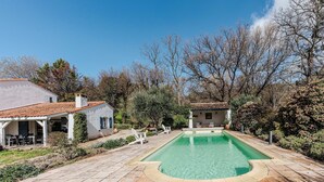 A swimming pool with a tiled deck, surrounded by trees and two buildings with tiled roofs. - Villa Triptyque - Avec piscine et grand jardin (Villecroze)
