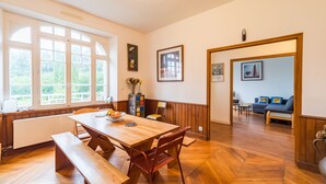 Ein Essbereich mit Holztisch und Bänken, einem Heizkörper und Blick ins Freie durch große Fenster.