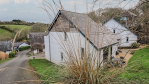Una casa blanca con techo inclinado, una chimenea visible y un pequeño porche.