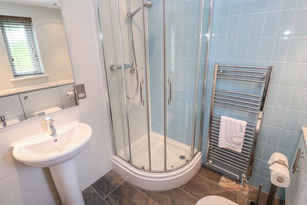 A bathroom with a glass-enclosed shower, a pedestal sink, a towel rack, and a toilet.