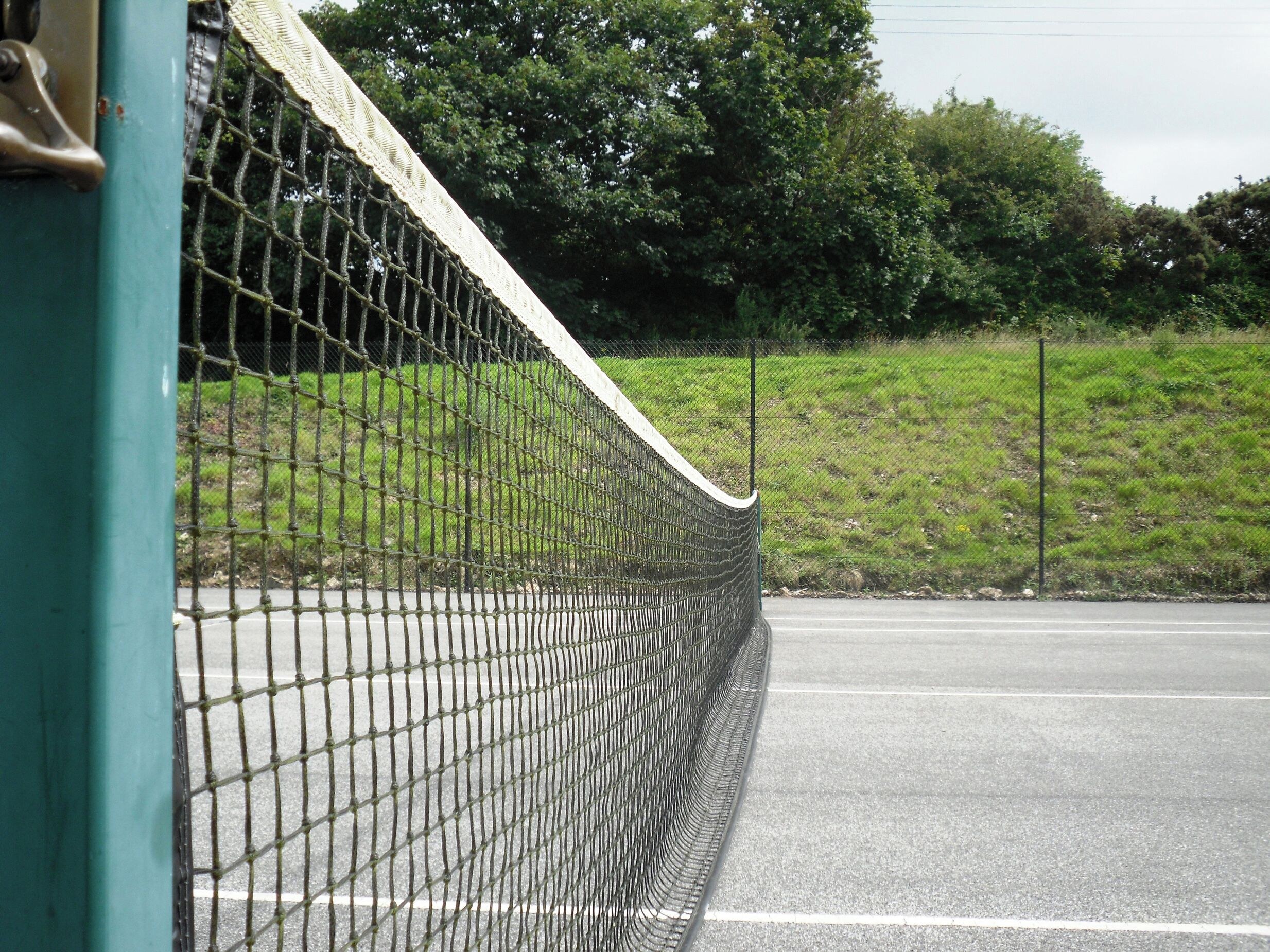 Een tennisbaan met een net, omgeven door een hek en groen.