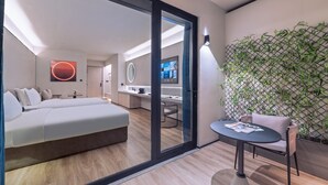 Habitación de hotel moderna con una cama grande, una mesita, una silla, un televisor, un espejo y una pared decorada con una planta de bambú.