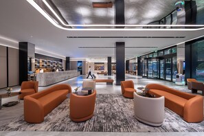 Un hall d'entrée moderne avec des sièges orange, un comptoir d'accueil et une grande entrée vitrée.