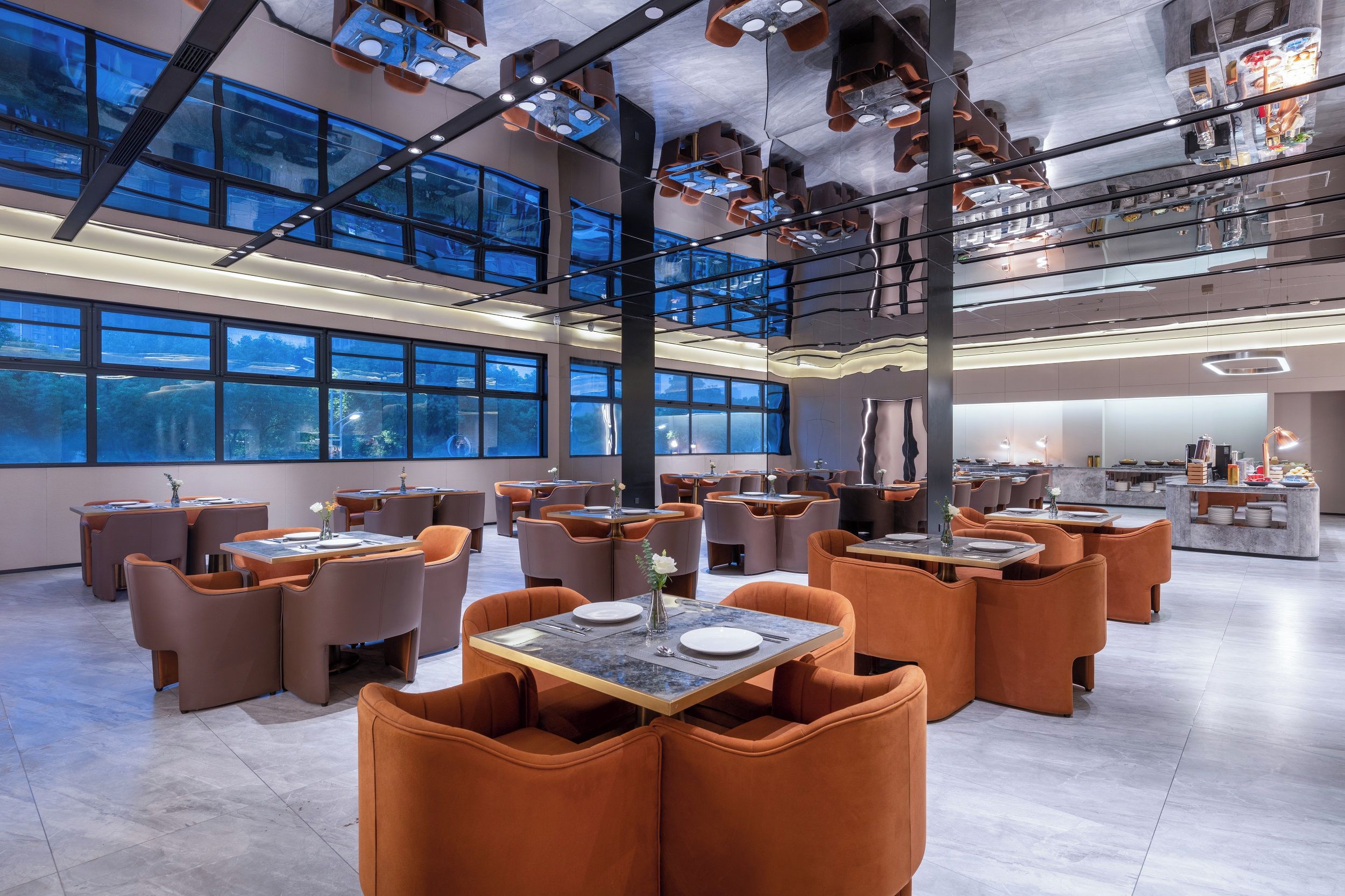 A modern restaurant with high ceilings, large windows, and orange seating. Tables are set with white plates and vases.