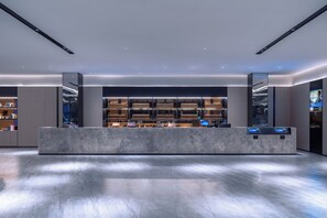 Een moderne hotellobby met een marmeren receptiebalie, een groot digitaal scherm en een goed verlicht interieur.