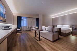 Une chambre d’hôtel moderne avec un plancher en bois, un canapé, un lit, une petite table et un téléviseur fixé au mur.