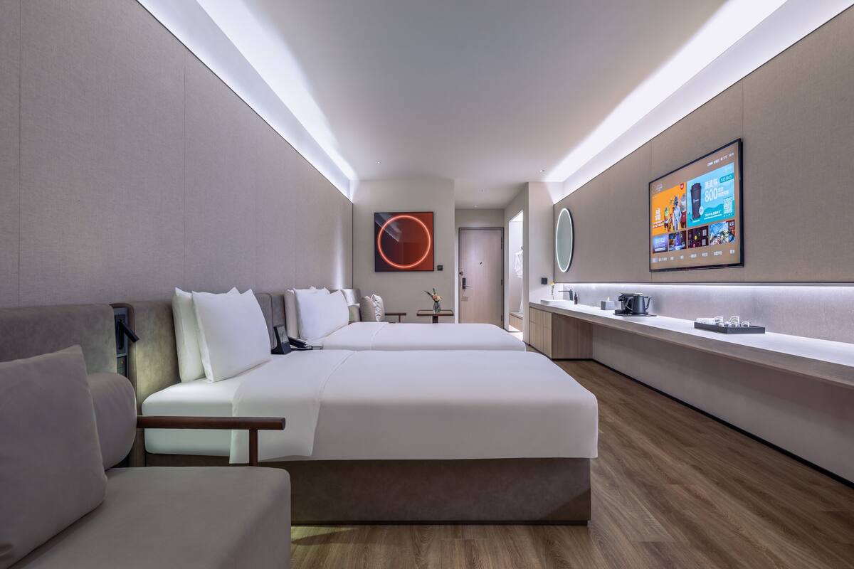 Une chambre d’hôtel moderne, dotée d’un grand lit, d’une table de chevet, d’une télévision et d’une salle de bain visible à travers une porte ouverte.