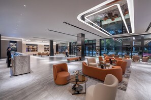 Un hall d’entrée spacieux, doté de mobilier moderne, d’un comptoir de réception et de grandes fenêtres offrant une vue sur l’extérieur.