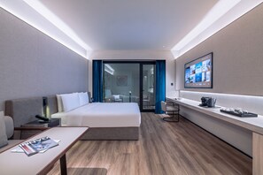 Una habitación de hotel moderna con una cama grande, un escritorio pequeño, un televisor montado en la pared y vistas al comedor a través de una puerta de vidrio.