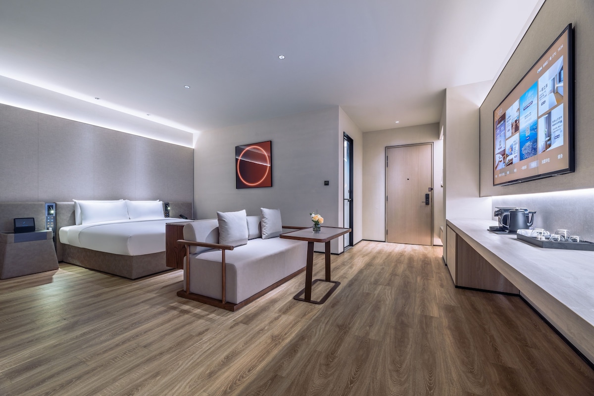 Ein modernes Hotelzimmer mit Bett, Sofa, Nachttisch und einer Küchenzeile mit Arbeitsfläche und Geräten.