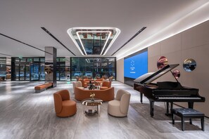 Un vestíbulo moderno con un piano de cola, asientos cómodos, una lámpara central llamativa y una gran pantalla digital que muestra el nombre de la marca.