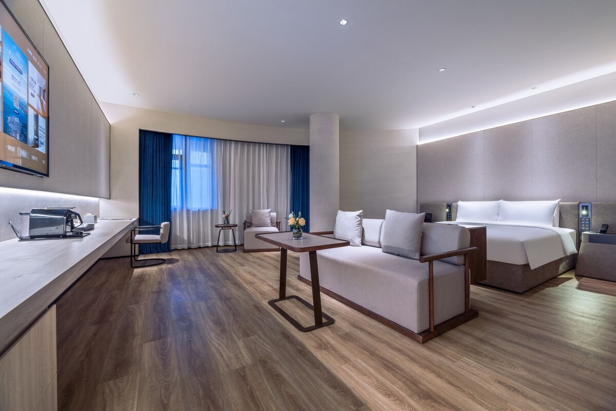 Une chambre d’hôtel moderne avec un plancher en bois, un canapé, un lit, un bureau avec un ordinateur portable et un téléviseur fixé au mur.